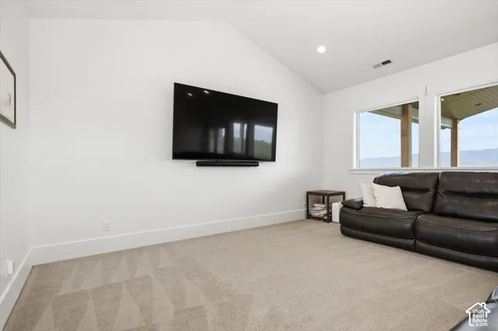 Vaulted ceiling, recessed lighting, carpeted flooring, wall-mounted television, and expansive windows
