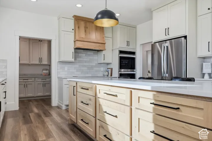 Kitchen featuring a wood-finish floor, light-toned shaker cabinetry, a wood range hood, a kitchen island with light wood cabinetry, and stainless steel appliances