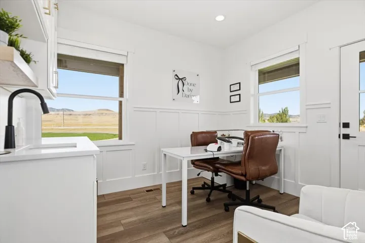 Bright room featuring wood-finish flooring, white paneled walls, and built-in white cabinetry with a matte black faucet