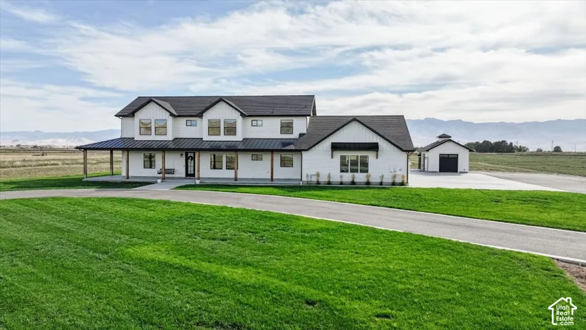 White exterior with black-framed windows, a covered front porch with wood columns, an attached garage, a detached garage, and a paved driveway