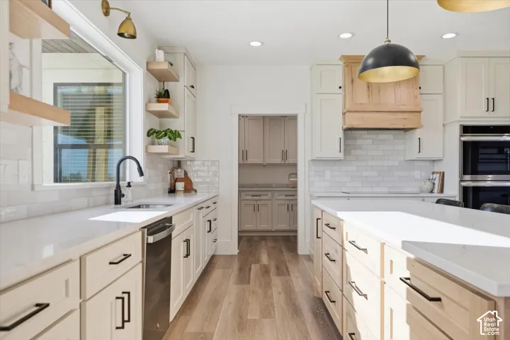 Kitchen featuring wood-finish flooring, white cabinetry, a built-in double oven, a center island with countertop seating, and a large window above the sink