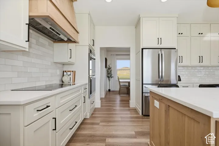 Kitchen featuring white shaker cabinetry, stainless steel appliances, light wood-finish flooring, a white subway tile backsplash, and light-colored countertops