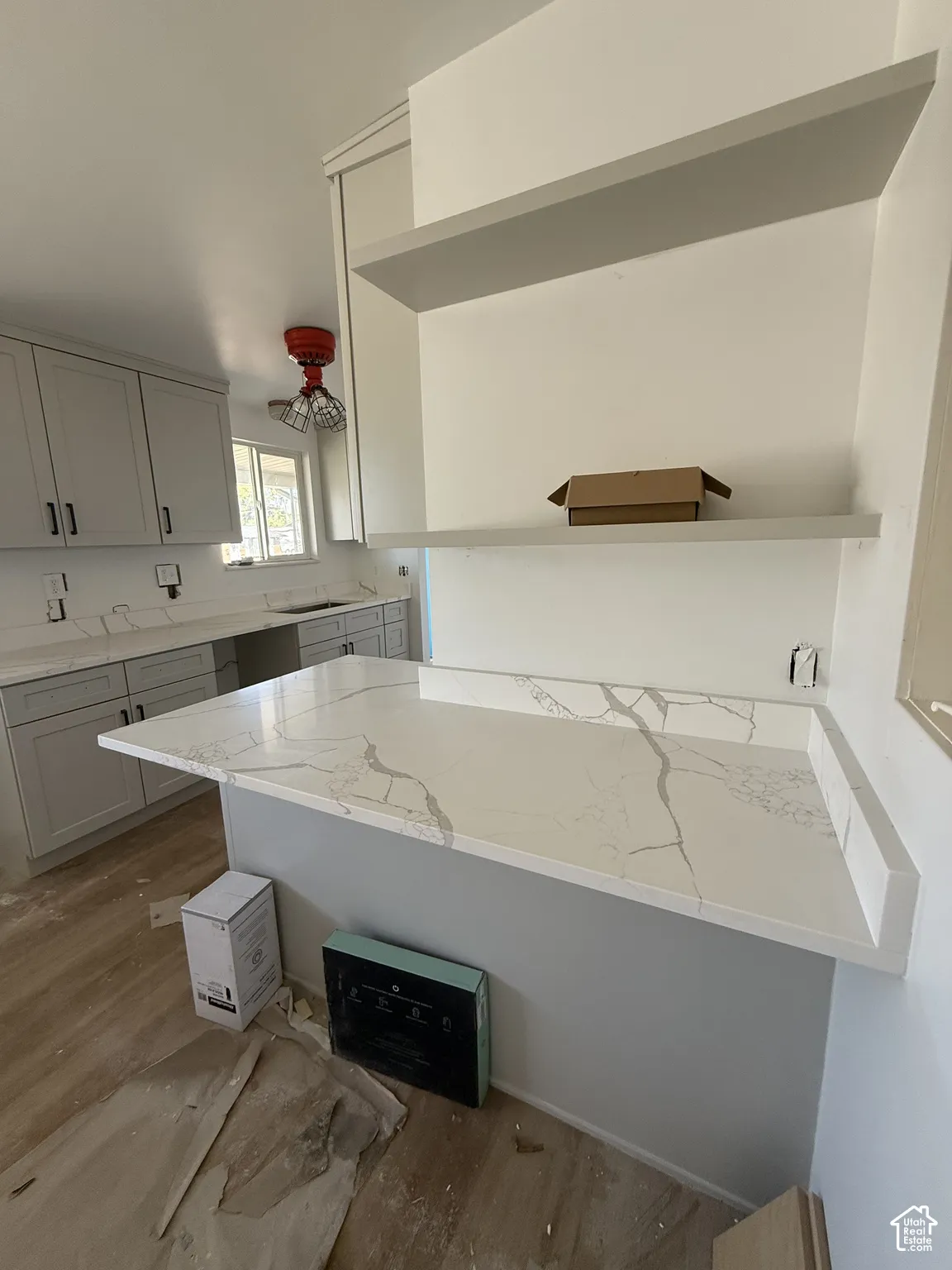 Kitchen featuring light gray cabinetry, white countertops with veining, an island with an extended counter, and wood-finish flooring