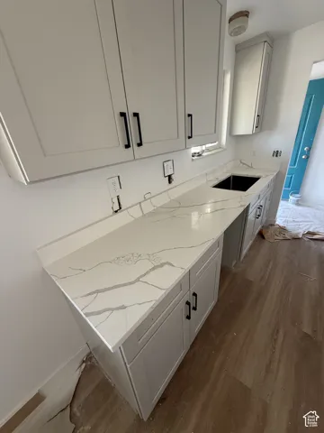 Light-toned cabinetry with modern black hardware, stone-finish countertops, an undermount sink, and wood-finish flooring