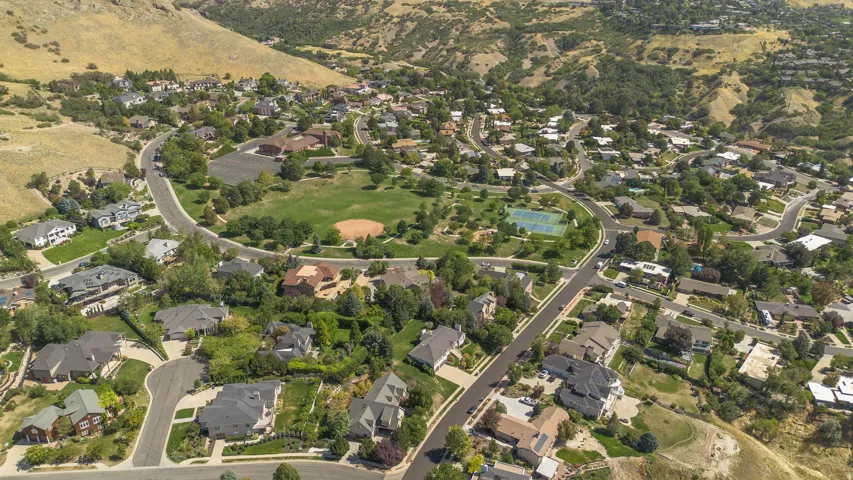 Expansive residential area featuring winding streets, abundant mature trees, a central park space with a baseball diamond, and tennis courts