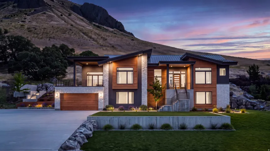 Modern architectural design featuring a multi-level exterior, extensive window placement, a two-car garage with a wood-finish door, and integrated outdoor lighting