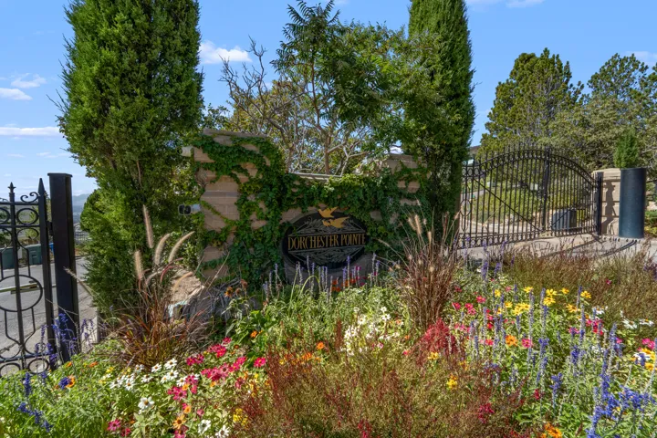 Entry gate featuring decorative wrought ironwork, stone pillars, and lush landscaping with varied plantings