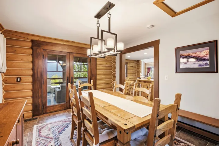 Dining area with exposed log walls, glass-paned double doors, and an open doorway to another room