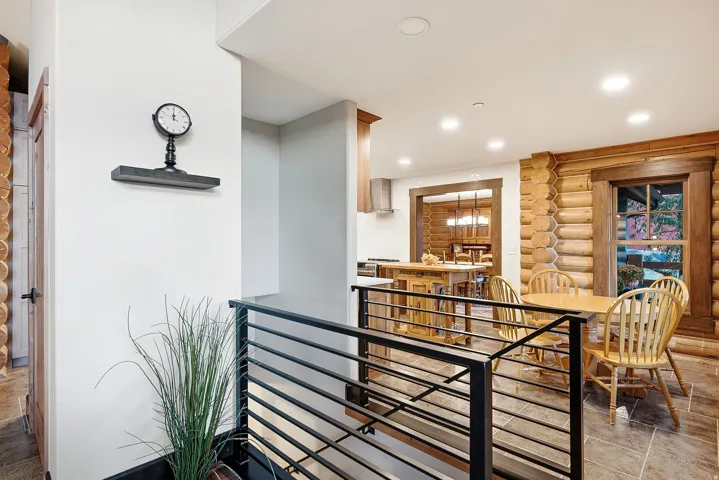 Open-concept living space with log wall accents, recessed lighting, and a modern horizontal metal railing