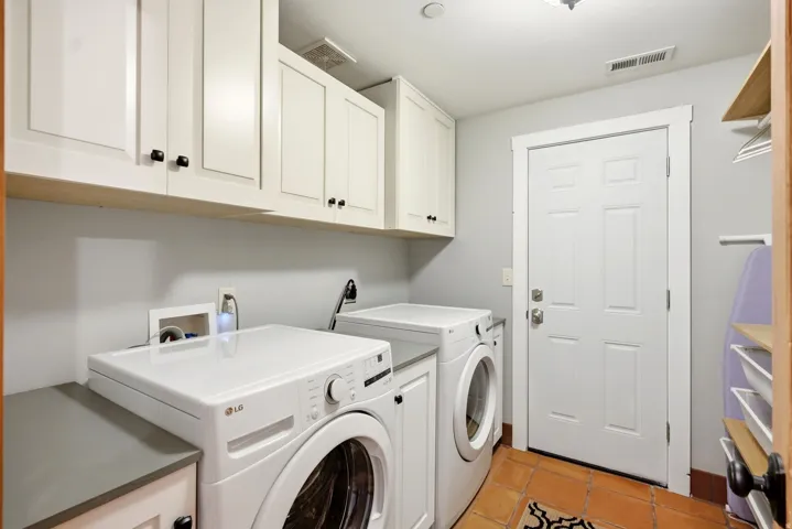 Functional laundry area featuring white shaker-style cabinetry, a built-in counter, and terra cotta-style flooring
