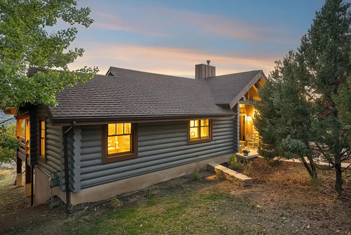 Log cabin exterior with a shingle roof, wood-framed windows, and a covered front entry