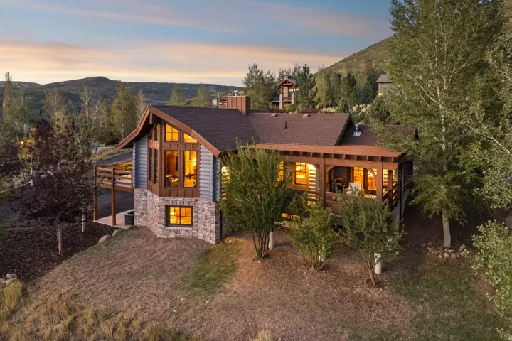 Stone and wood-sided exterior featuring a gable roof, covered deck, and exposed wood beam accents