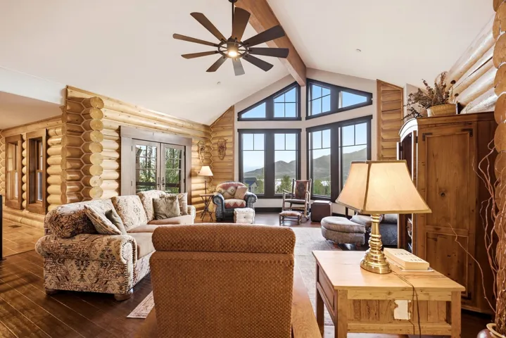 Vaulted ceiling featuring exposed beams, log wall construction, dark wood-finish flooring, and large picture windows