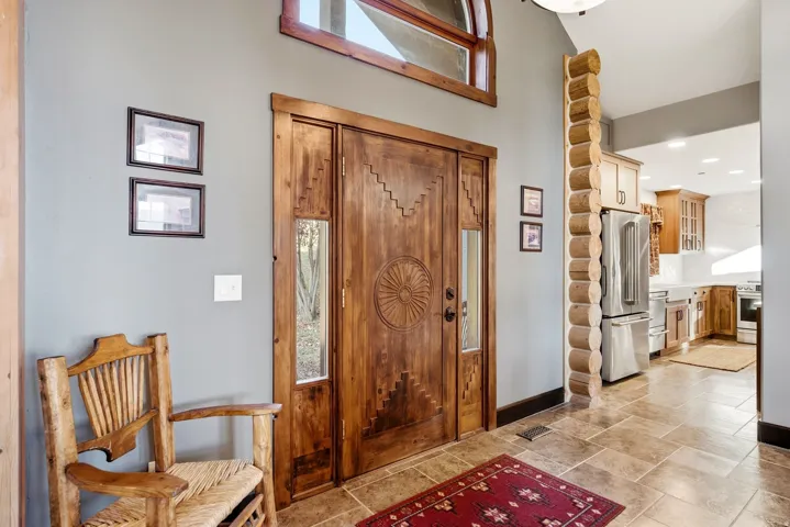 Custom carved wood entry door with sidelights, transom window, log structural element, and tile flooring