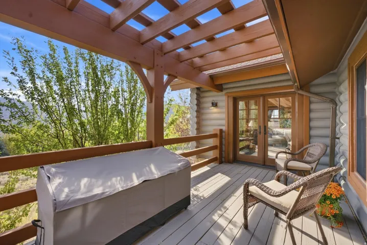 Exterior deck with a wood pergola, log siding, and double glass-panel doors