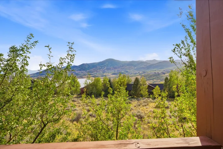 Expansive mountain scenery with a distant body of water, foreground greenery, and a visible structure