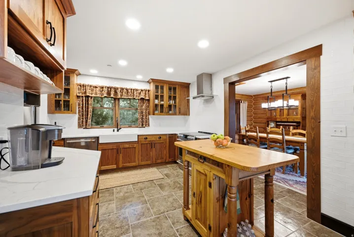 Wood cabinetry with black hardware, white countertops, farmhouse sink, stainless steel range hood, and tile flooring