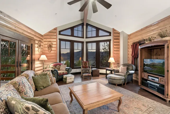 Vaulted ceiling with a ceiling fan, log-style wall finishes, a wall of windows, French doors, and wood-finish flooring