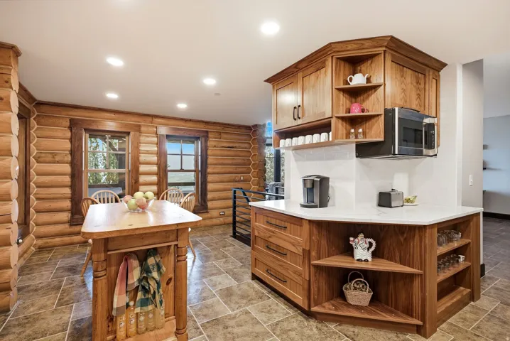 Log-style wall construction, tiled flooring, wood-finish cabinetry, white countertops, and recessed ceiling lighting