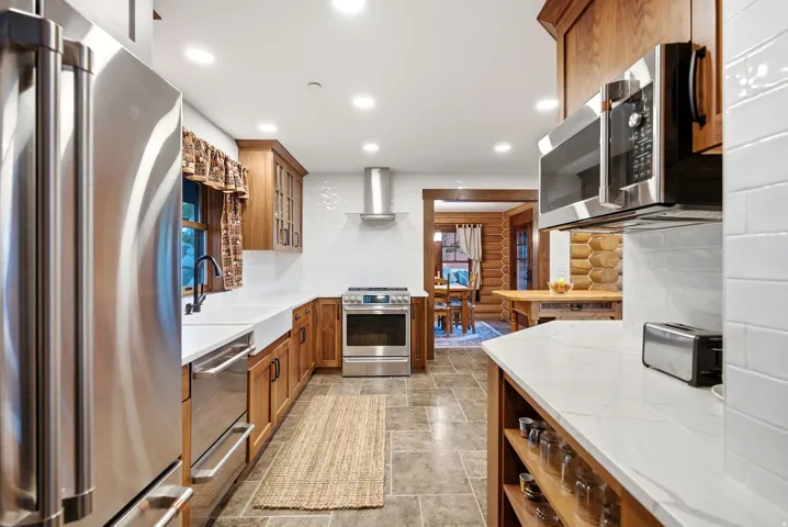 Stainless steel appliances, white subway tile backsplash, white countertops, wood cabinetry, and recessed lighting