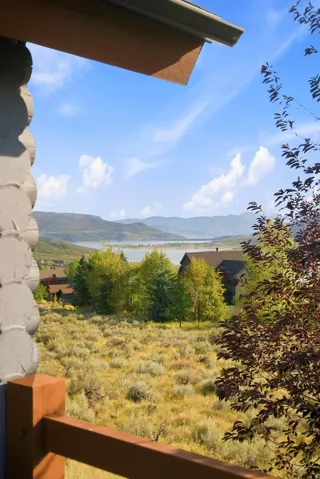 Expansive mountain scenery with a distant lake, surrounded by natural landscaping, and featuring a wood railing
