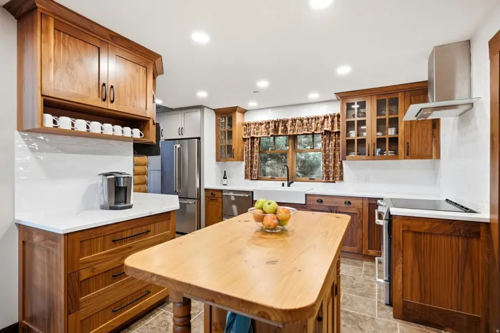 Wood cabinetry with integrated appliances, white subway tile backsplash, and a large farmhouse sink