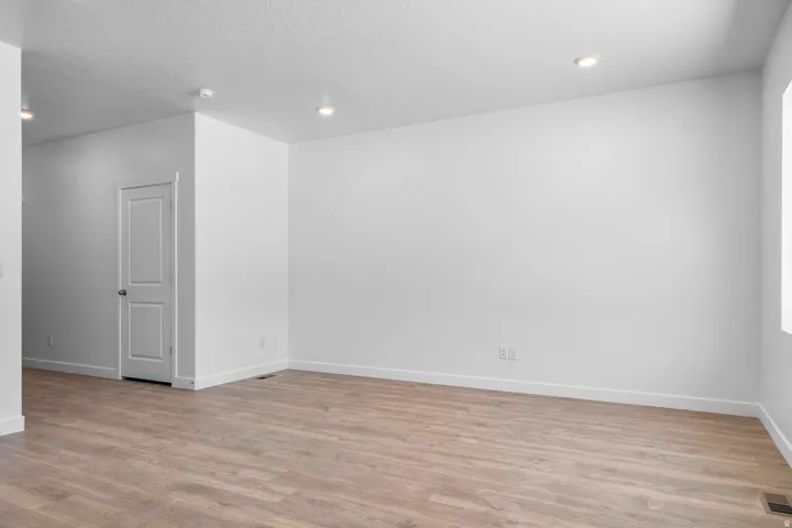 Spacious room featuring wood-finish flooring, white painted walls, recessed lighting, and a white interior door