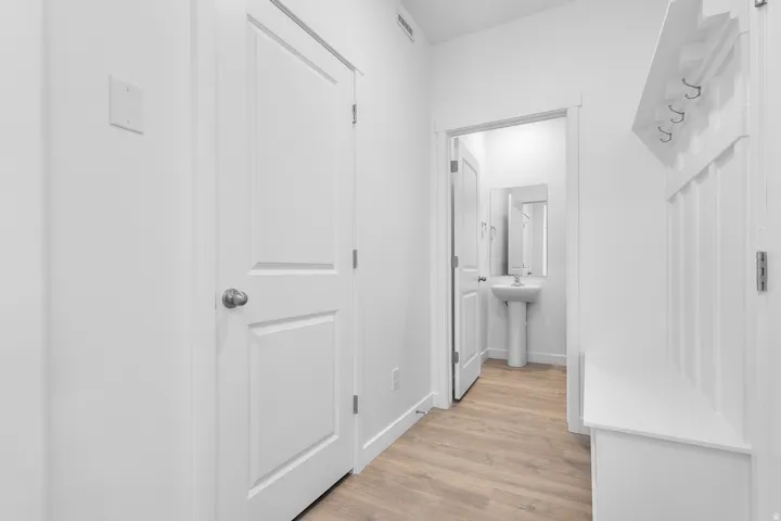 Wood-finish flooring, white panel doors, built-in hall tree with storage bench, and a pedestal sink with a mirror
