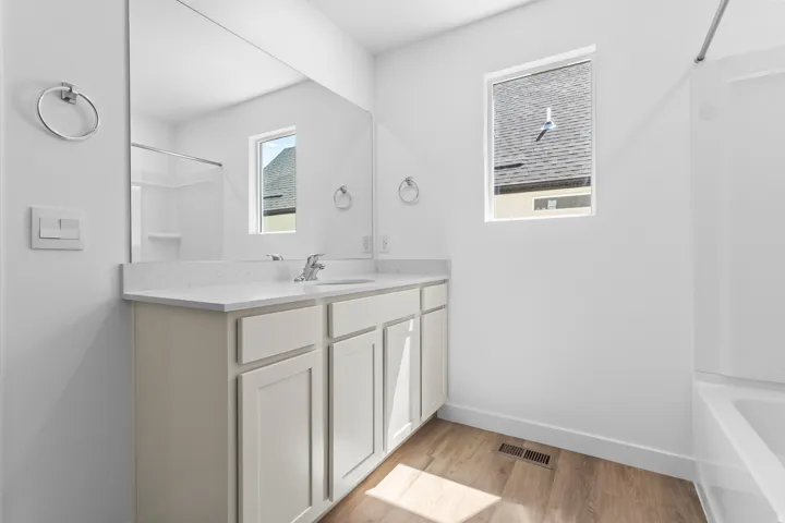 White vanity with a light-toned countertop, a rectangular mirror, a window providing natural illumination, and wood-finish flooring