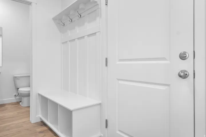 Entryway featuring a built-in bench with cubbies, wall-mounted coat hooks, and wood-finish flooring