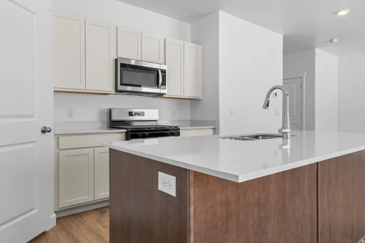Kitchen featuring a stainless steel range, microwave, light cabinetry, and an island with a built-in sink and pull-down faucet