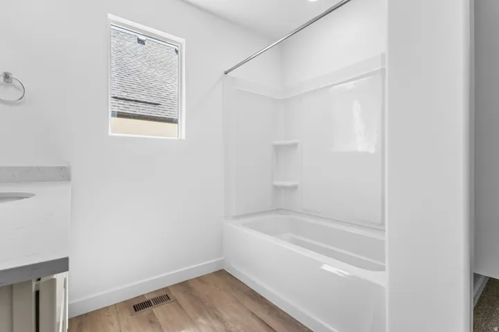 Tub-shower combination with integrated shelving, wood-finish flooring, and a window for natural light