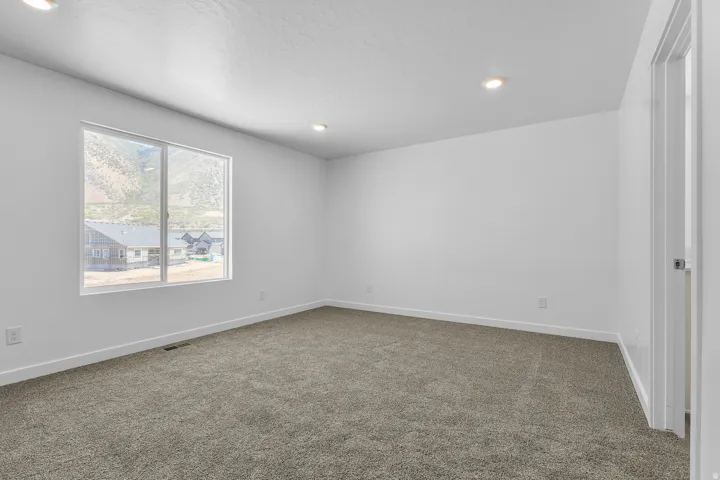 Recessed ceiling lighting, white painted walls, gray carpeted flooring, and a sliding window
