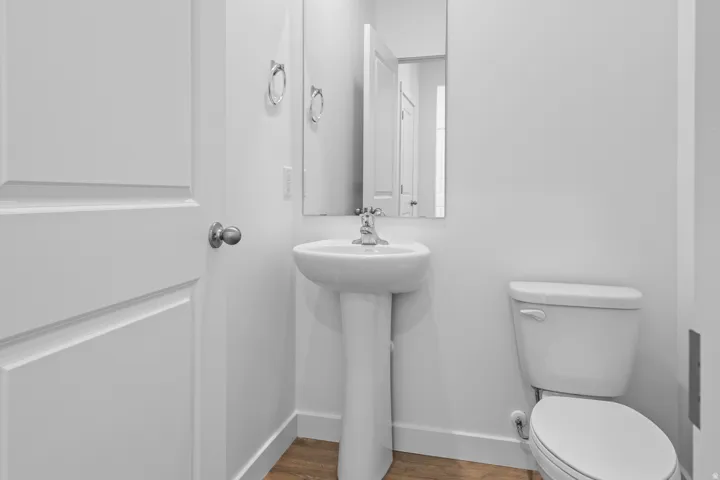 Pedestal sink with chrome faucet, wall-mounted mirror, and wood-finish flooring