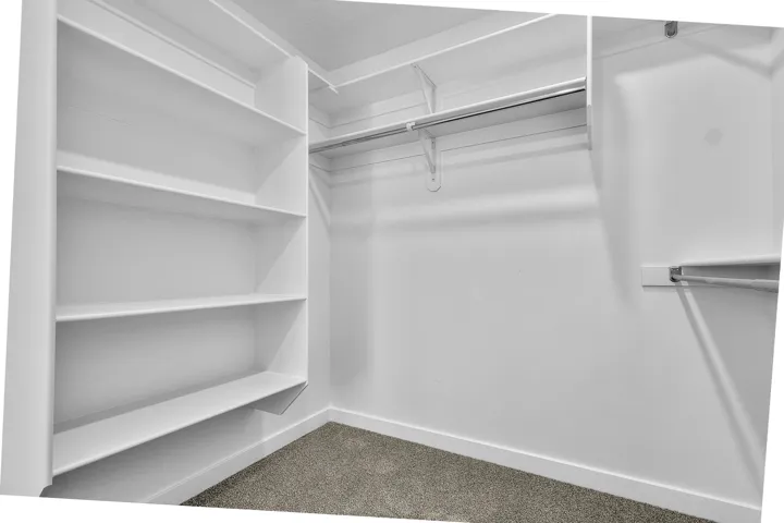 Walk-in closet featuring built-in shelving, multiple hanging rods, and carpet flooring
