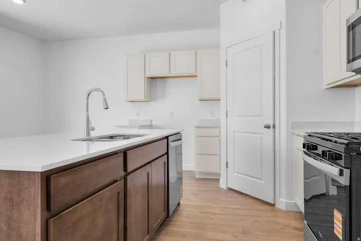 Kitchen featuring wood-finish flooring, two-tone cabinetry, stainless steel appliances, a kitchen island with an integrated sink, and white countertops