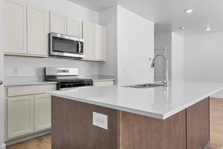 Kitchen featuring white shaker-style cabinetry, stainless steel appliances, a center island with an integrated sink, and light-toned countertops