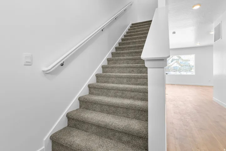 Carpeted staircase with a white handrail, leading to an upper level