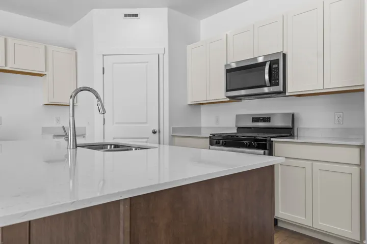 Kitchen featuring a large island with an undermount sink and gooseneck faucet, light-toned cabinetry, stainless steel microwave, and gas range