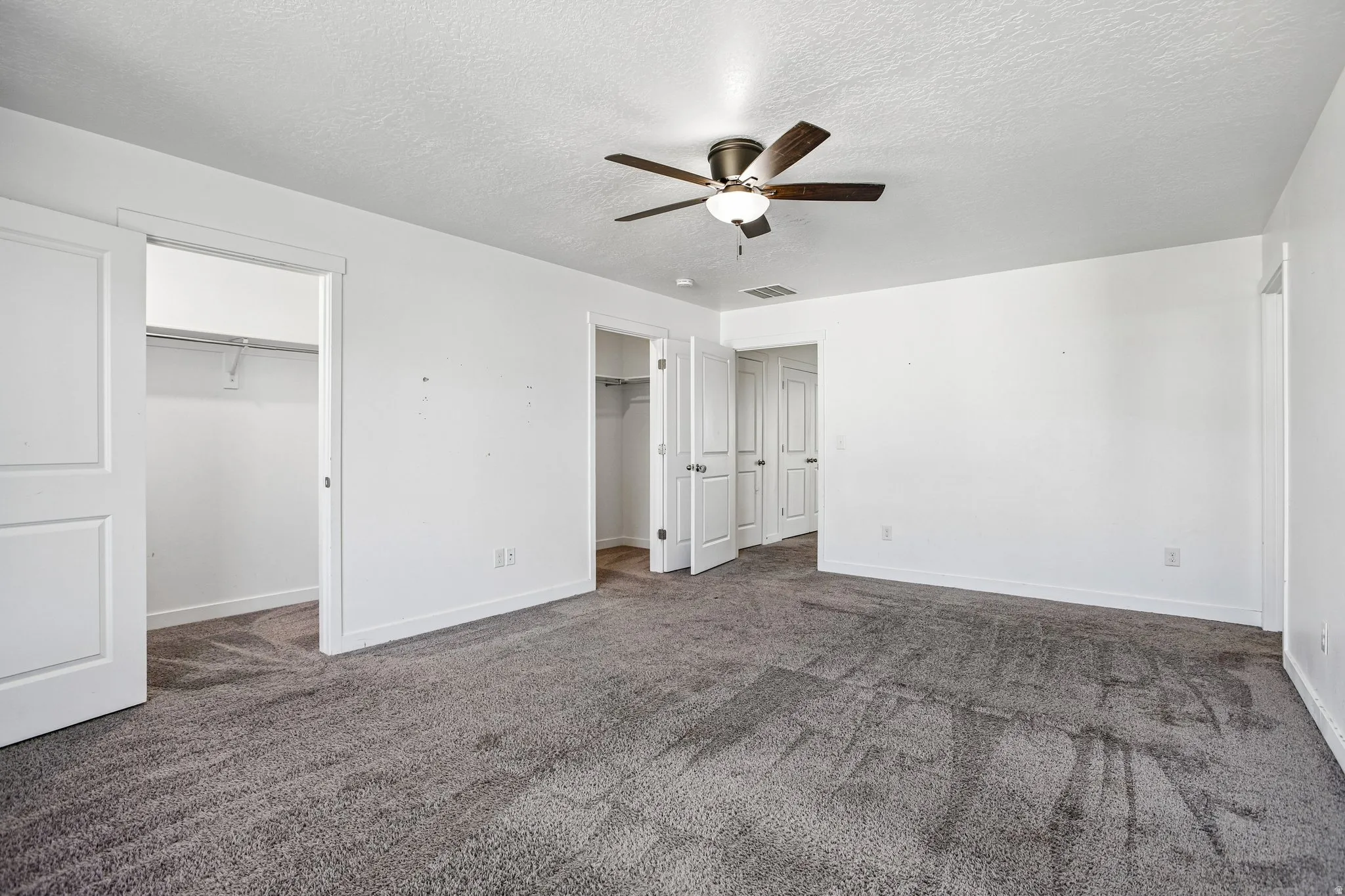 Spacious interior featuring neutral carpeting, white walls, and a ceiling fan with integrated lighting
