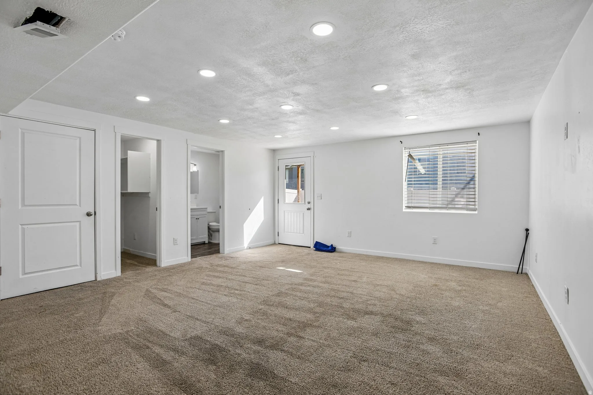 Spacious room featuring neutral carpeting, a white door with paneling, recessed lighting, and a window with horizontal blinds