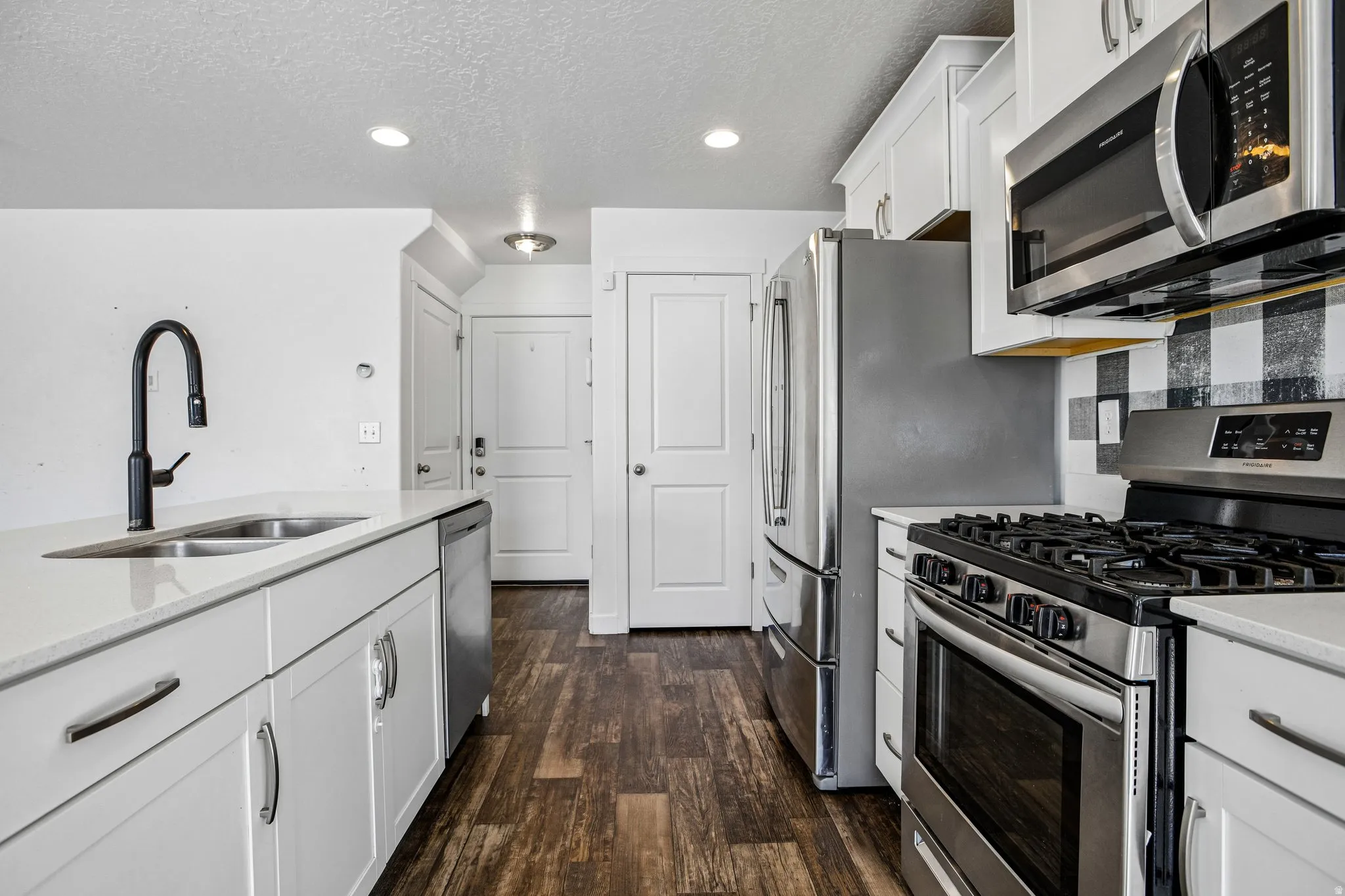 Kitchen featuring stainless steel appliances, white cabinetry, a black and white checkered backsplash, and wood-finish flooring