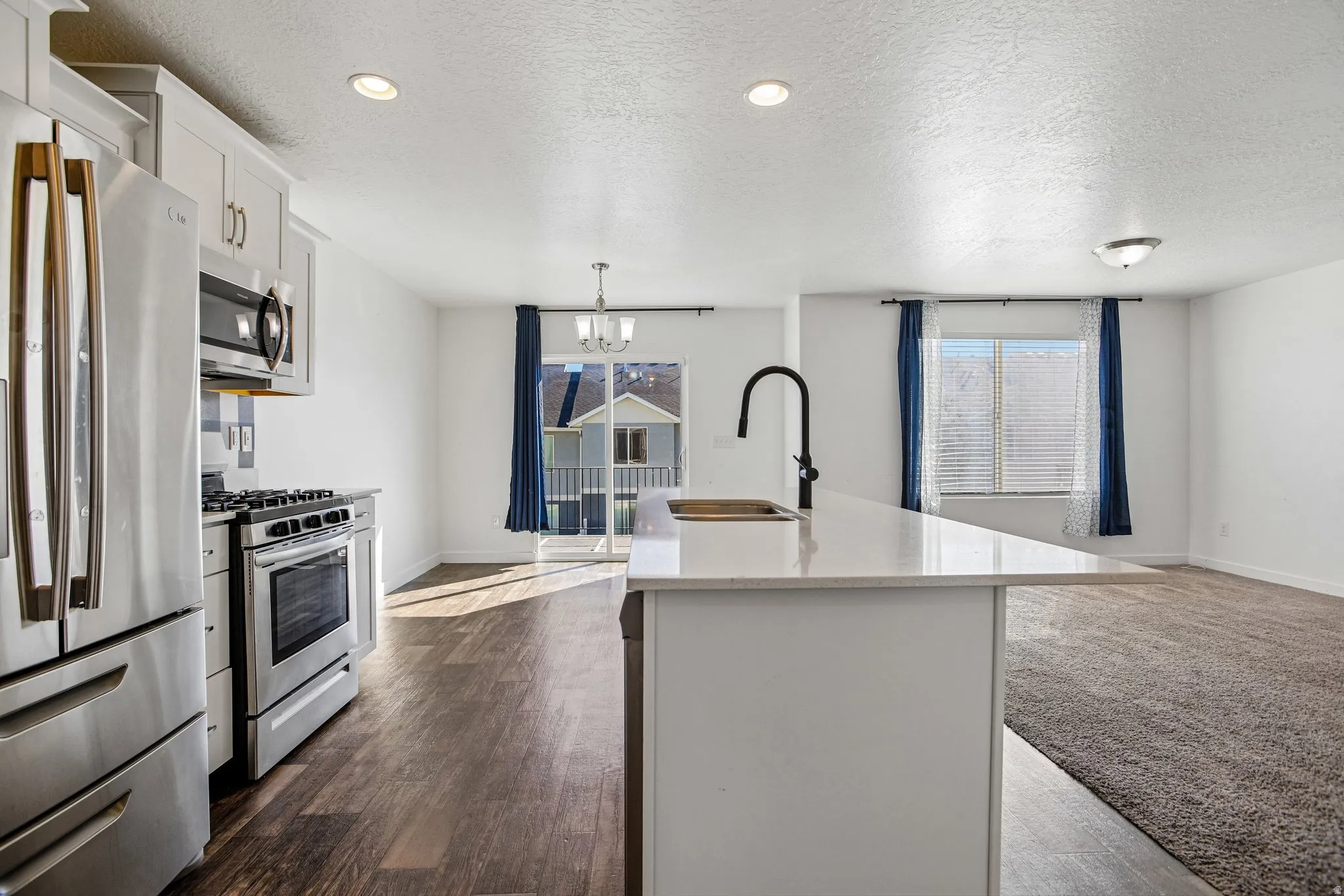 Kitchen featuring stainless steel appliances, white cabinetry, a kitchen island with a sink, and wood-finish flooring