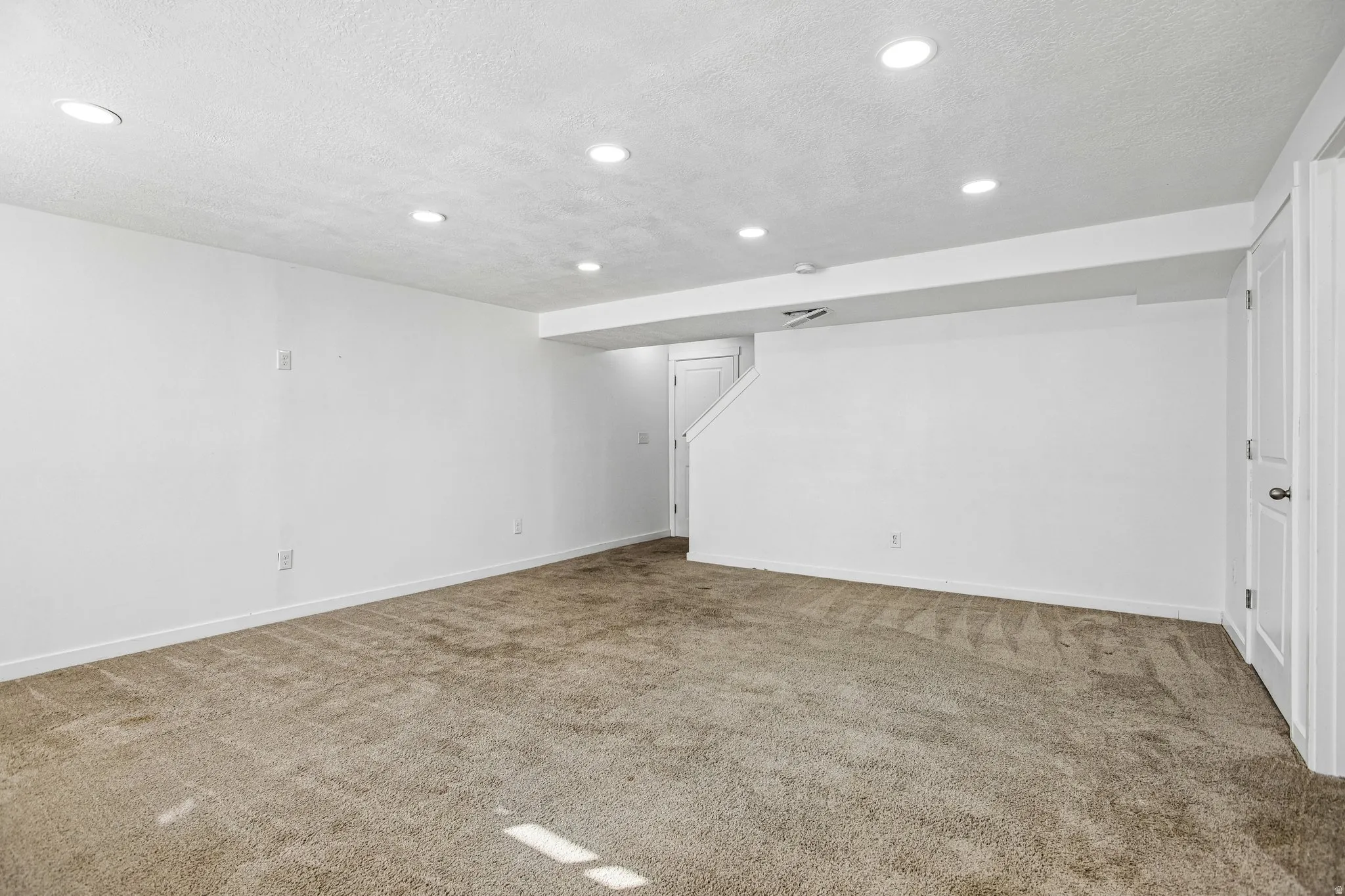 Neutral carpet flooring, recessed ceiling lighting, bright white walls, white trim, and a white interior door