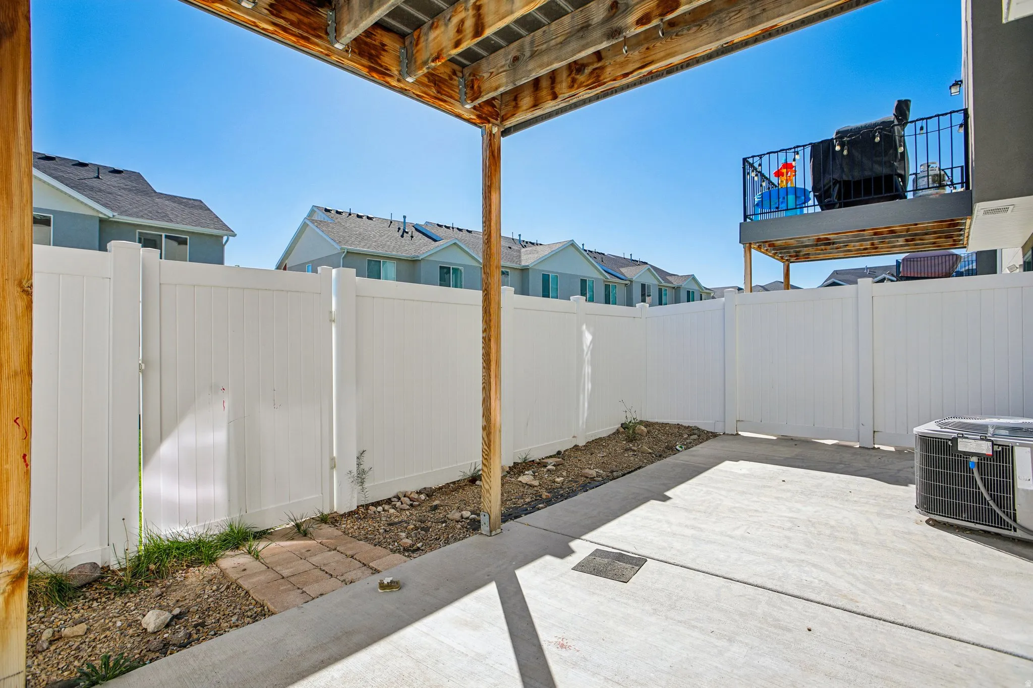 Private patio with concrete flooring, white privacy fencing, and a built-in deck overhead