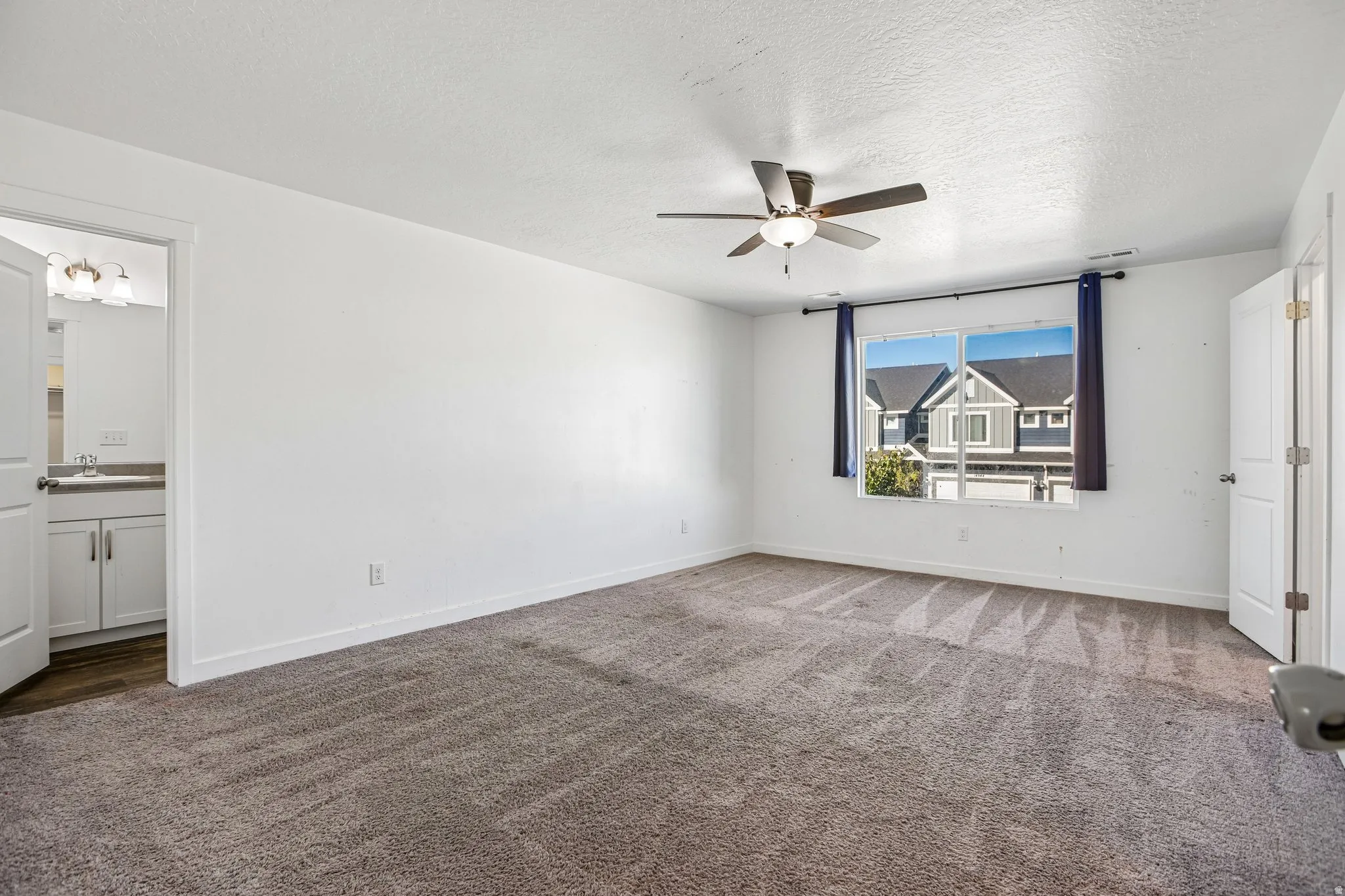 Spacious room with carpeted flooring, a ceiling fan with integrated lighting, and a large window