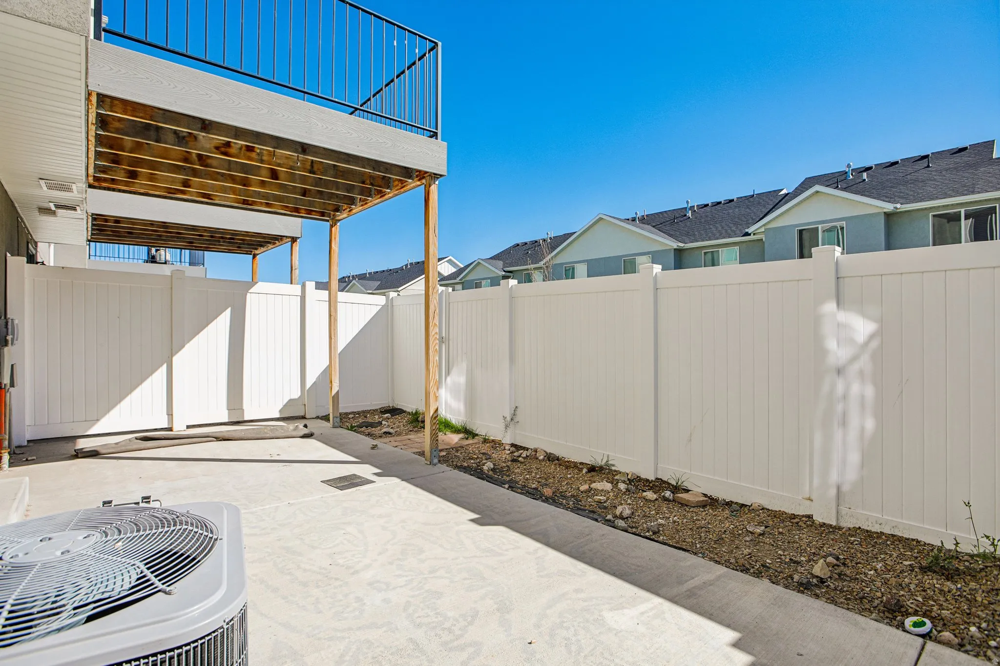 Outdoor patio with a concrete surface, overhead balcony, and perimeter fencing