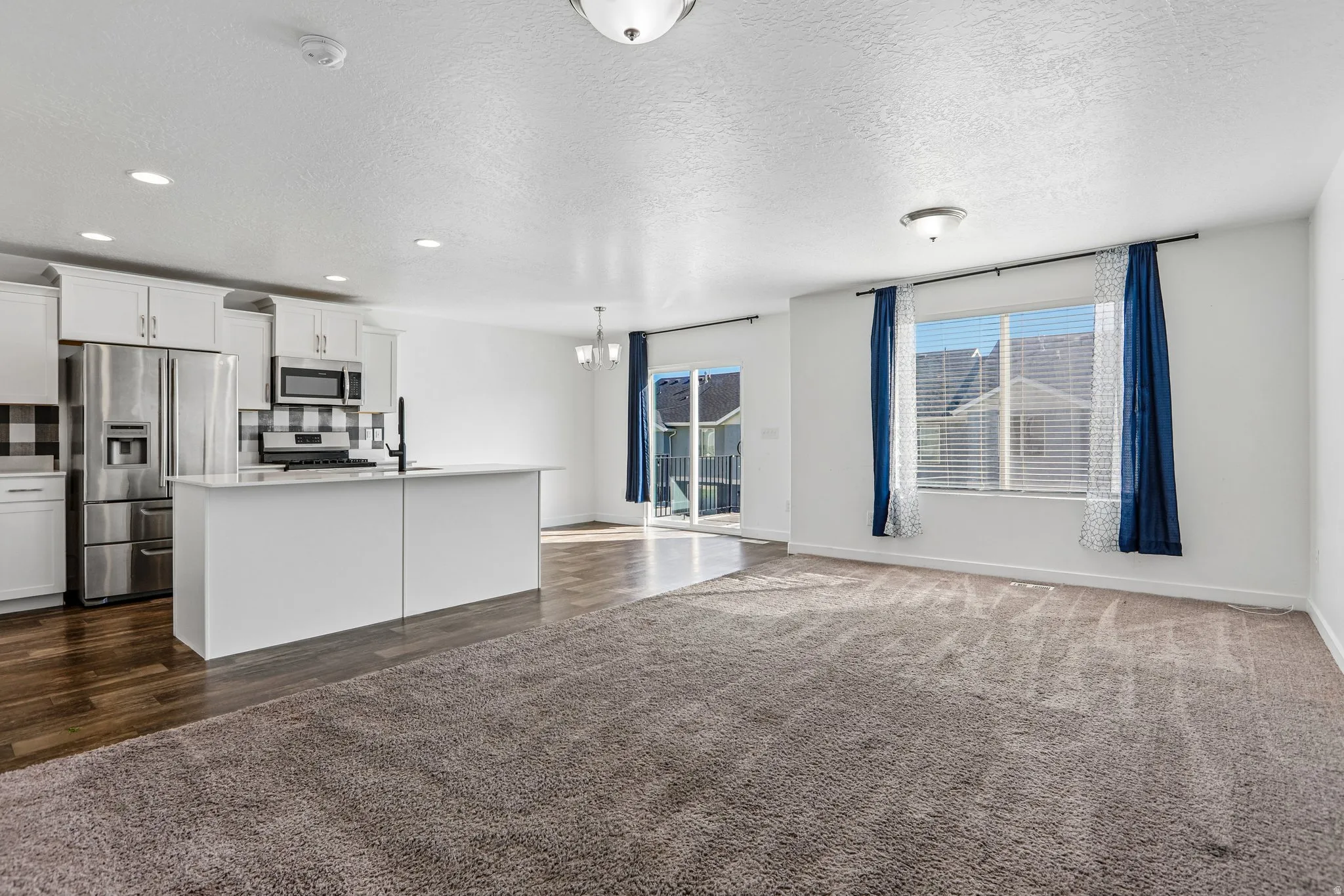 Open concept living area featuring a kitchen island, stainless steel appliances, wood-finish flooring, and a sliding glass door