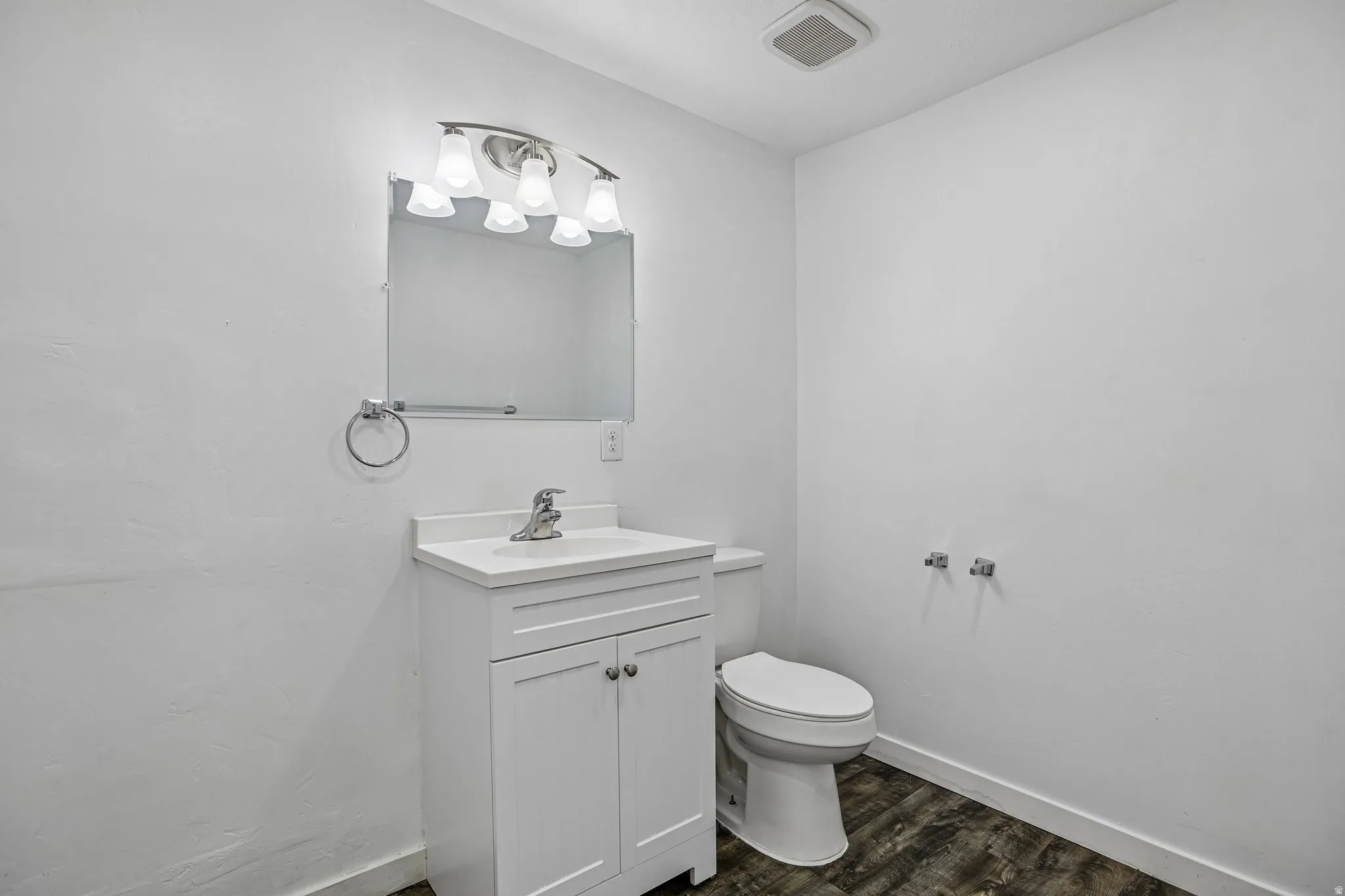 White vanity with integrated sink, chrome faucet, and wood-finish flooring