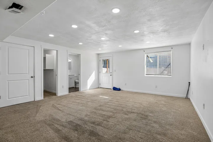 Spacious room featuring neutral carpeting, a white door with paneling, recessed lighting, and a window with horizontal blinds